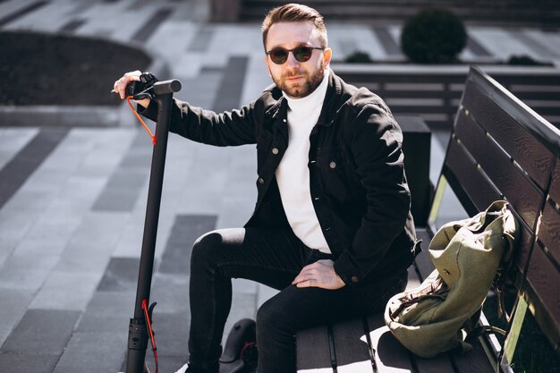 Giovane uomo bello seduto sulla panchina nel parco, a riposo da un giro in scooter