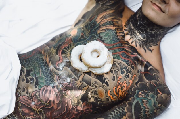 giovane uomo bello tatuato facendo colazione a letto all&#39;aperto all&#39;aperto nel giardino