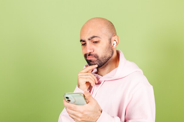 Giovane uomo caucasico calvo in felpa con cappuccio rosa isolato, tenere premuto il mento premuroso tenere il telefono