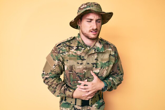 Giovane uomo caucasico che indossa l'uniforme dell'esercito mimetico con la mano sullo stomaco perché indigestione, malattia dolorosa sensazione di malessere. concetto di dolore.