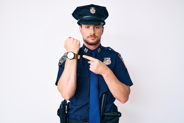 Giovane uomo caucasico che indossa l'uniforme della polizia in fretta che punta a guardare il tempo, l'impazienza, guardando la telecamera con espressione rilassata