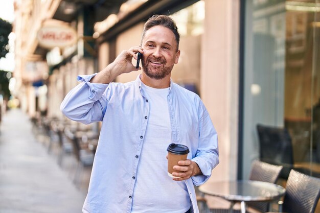 Giovane uomo caucasico che parla sullo smartphone bevendo caffè sulla terrazza della caffetteria