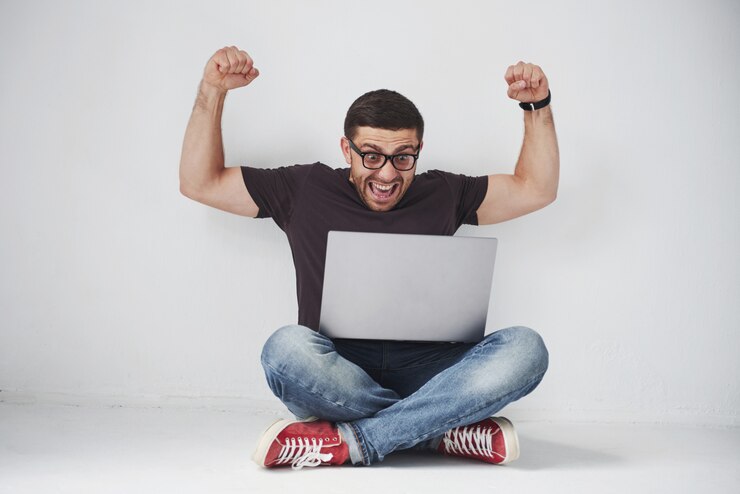 Foto gratuito giovane uomo caucasico che si siede sopra il muro di mattoni bianco facendo uso del computer portatile