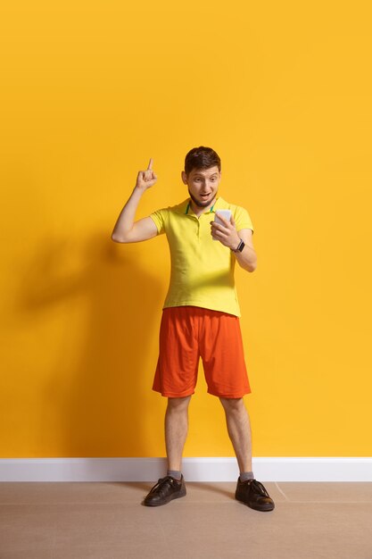 Giovane uomo caucasico che utilizza il ritratto completo di lunghezza del corpo dello smartphone isolato sopra la parete gialla