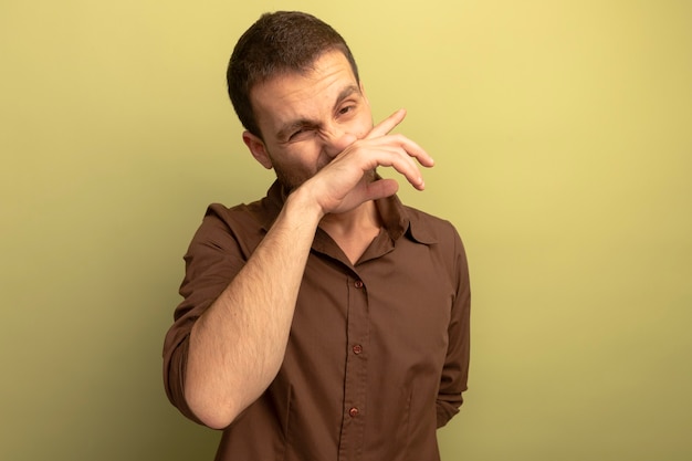 Giovane uomo caucasico guardando la telecamera pulendosi il naso con la mano isolata su sfondo verde oliva con spazio di copia