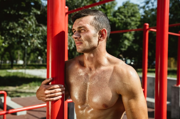 Giovane uomo caucasico senza camicia muscolare mentre fa il suo allenamento su barre orizzontali