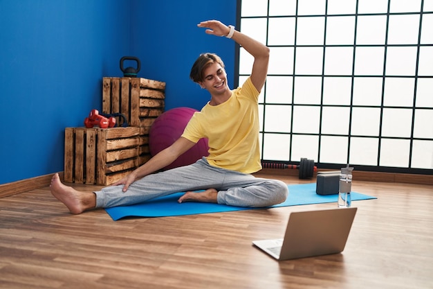 Giovane uomo caucasico sorridente fiducioso avendo lezione di stretching online al centro sportivo