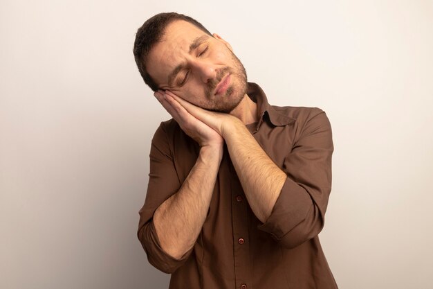 Giovane uomo caucasico stanco che fa gesto di sonno isolato su priorità bassa bianca con lo spazio della copia