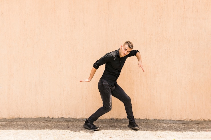 Foto gratuito giovane uomo che balla hip-hop contro il muro beige