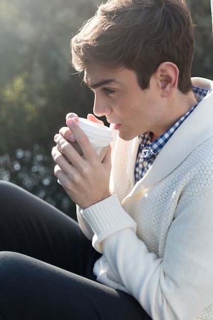 Giovane uomo che beve caffè caldo al tramonto