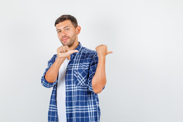 Giovane uomo che indica i pollici a lato e sorridente in camicia, vista frontale.