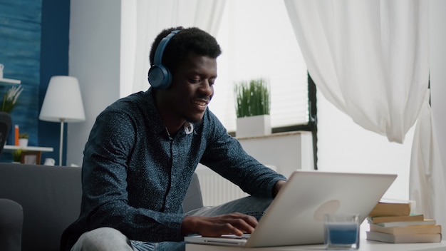 Giovane uomo che indossa le cuffie, digita sul laptop, utilizza i servizi online web di Internet