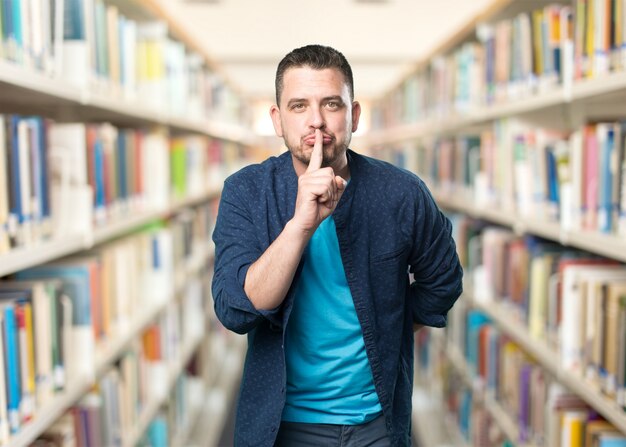 Giovane uomo che indossa un vestito blu. Facendo il gesto di silenzio.