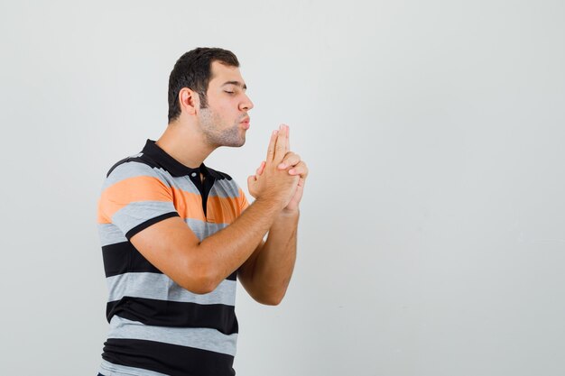 Giovane uomo che mostra il gesto della pistola in maglietta e guardando concentrato, vista frontale. spazio per il testo