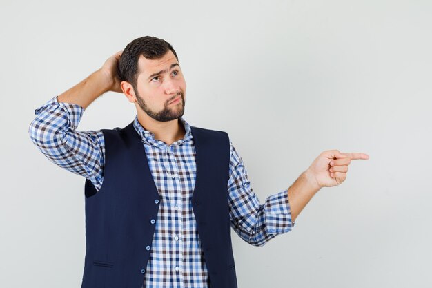 Giovane uomo che punta al lato in camicia, gilet e guardando pensieroso.