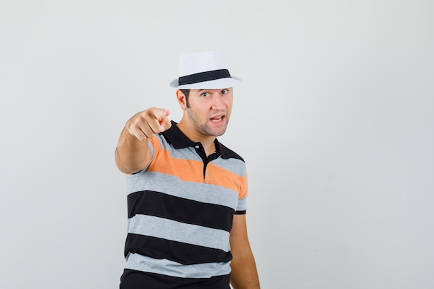 Giovane uomo che punta alla telecamera in t-shirt, cappello e guardando assicurato