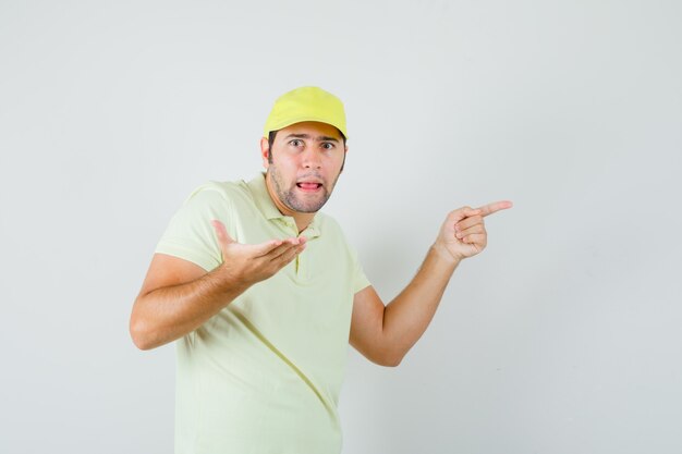 Giovane uomo che punta di lato in berretto di t-shirt e guardando perplesso