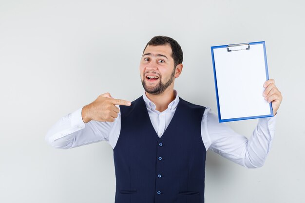 Giovane uomo che punta il dito negli appunti in camicia, gilet e guardando fiducioso