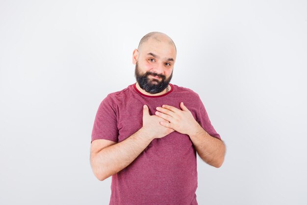 Giovane uomo che riposa le mani sul petto in maglietta rosa e sembra ottimista, vista frontale.