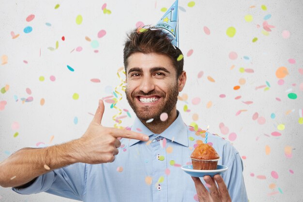 Giovane uomo circondato da coriandoli tenendo cupcake