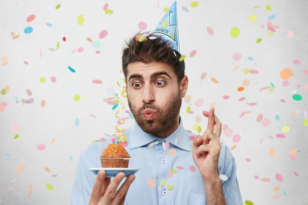 Giovane uomo circondato da coriandoli tenendo cupcake