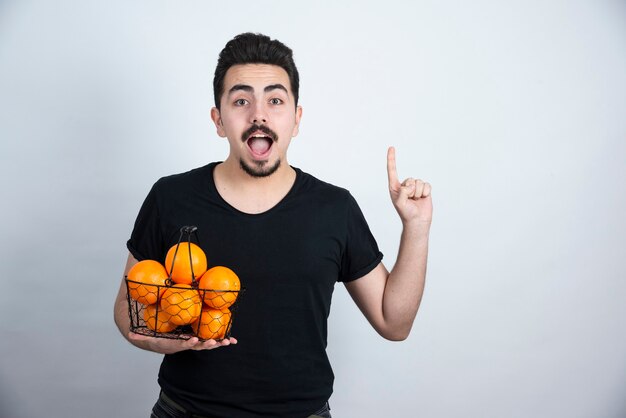 giovane uomo con cesto metallico pieno di frutti arancioni rivolto verso l'alto.