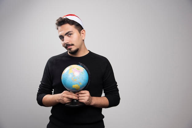 Giovane uomo con il cappello di Babbo Natale in possesso di un globo.