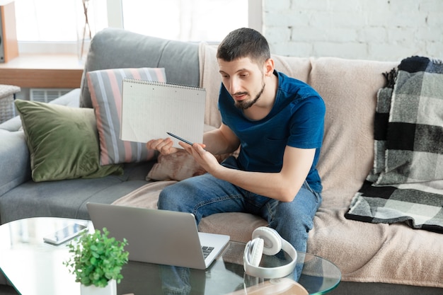 Giovane uomo concentrato che studia a casa durante i corsi online o informazioni gratuite da solo