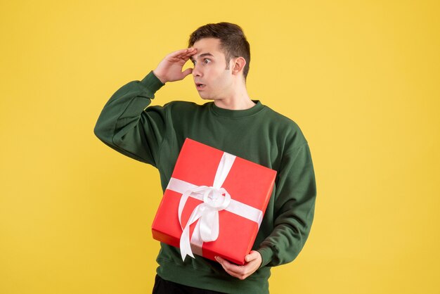 Giovane uomo confuso vista frontale con maglione verde in piedi sul giallo