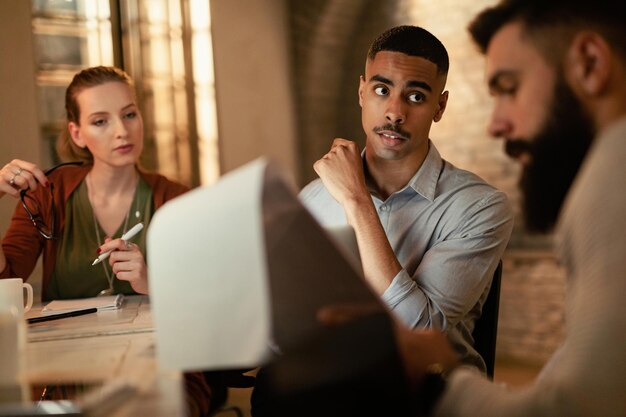 Giovane uomo d'affari afroamericano ei suoi colleghi esaminano i rapporti su una riunione in ufficio