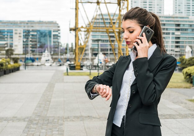 Giovane uomo d&#39;affari che controlla tempo sull&#39;orologio mentre parla sul telefono cellulare