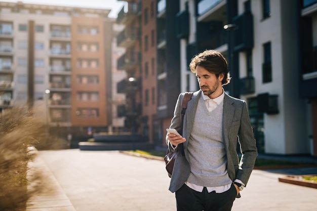 Giovane uomo d'affari che legge un messaggio di testo su smart phone per strada