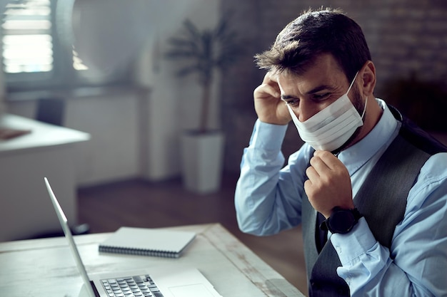 Giovane uomo d'affari che si protegge con la maschera mentre lavora in ufficio durante l'epidemia di coronavirus