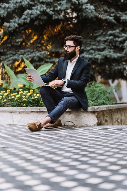 Giovane uomo d&#39;affari che si siede all&#39;aperto usando il computer portatile