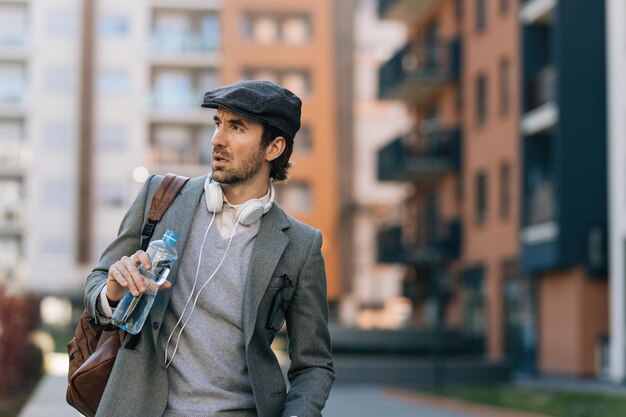 Giovane uomo d'affari con una bottiglia d'acqua che cammina in città e distoglie lo sguardo