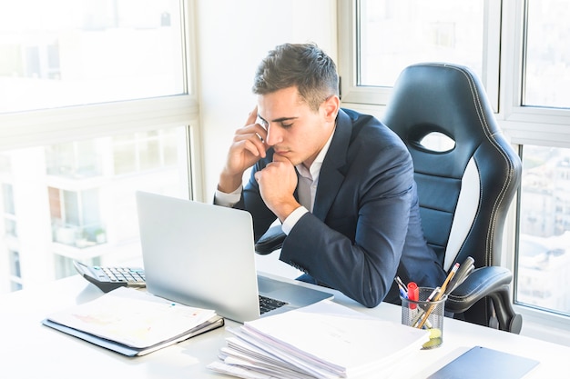 Giovane uomo d&#39;affari premuroso che esamina computer portatile nel luogo di lavoro