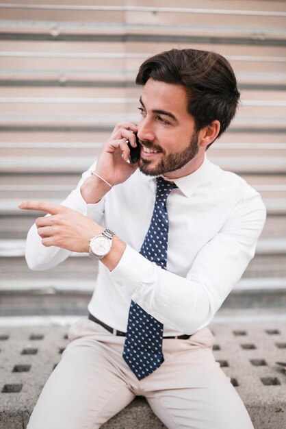 Giovane uomo d&#39;affari sorridente che gesturing mentre parlando sullo smartphone