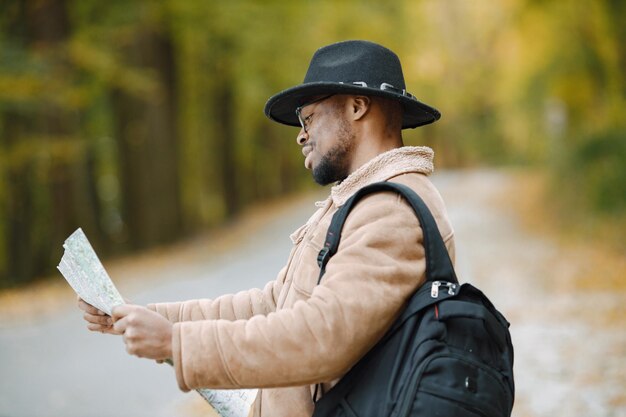 Giovane uomo di colore che fa l'autostop sulla strada e guarda la mappa. Viaggiatore maschio che si sente perso, viaggia da solo in autostop