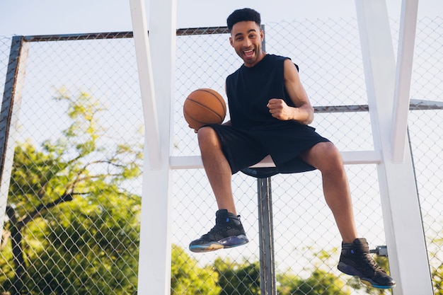 Giovane uomo di colore che fa sport, gioca a basket, stile di vita attivo, mattina d'estate, sorridendo felice divertendosi