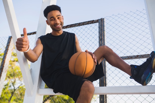 Giovane uomo di colore che fa sport, gioca a basket, stile di vita attivo, mattina d'estate, sorridendo felice divertendosi