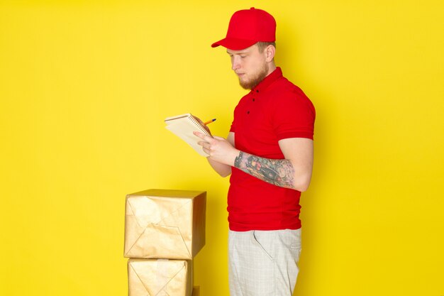 giovane uomo di consegna in polo rosso berretto rosso jeans bianchi scrivendo sul ripartitore giallo