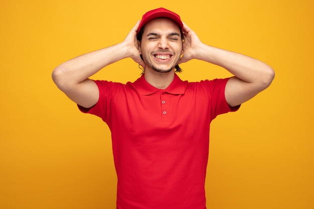 giovane uomo di consegna irritato che indossa uniforme e cappuccio che chiude le orecchie con le mani con gli occhi chiusi isolati su sfondo giallo