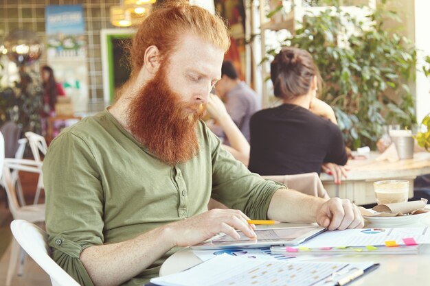 Giovane uomo di zenzero utilizzando tablet nella caffetteria