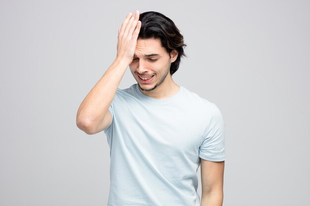 giovane uomo dispiaciuto che tiene la mano sulla testa guardando in basso isolato su sfondo bianco