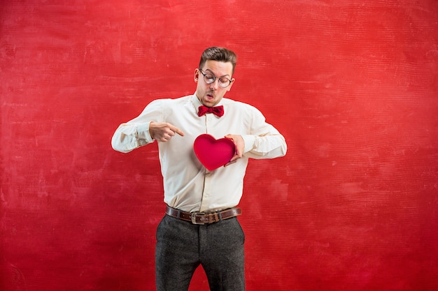 giovane uomo divertente con cuore astratto e orologio su sfondo rosso studio.