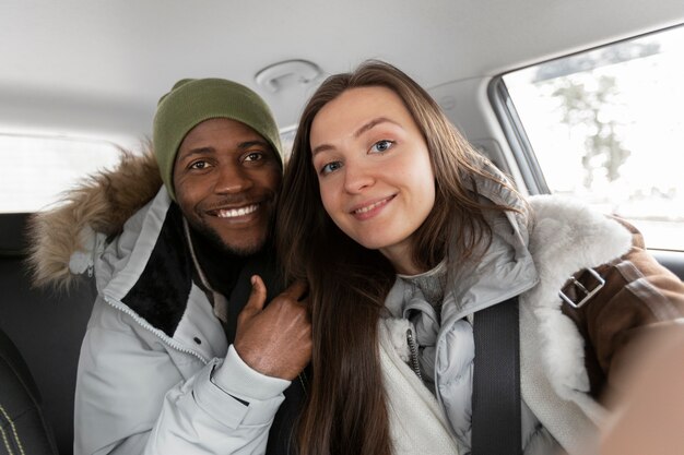 Giovane uomo e donna in macchina che si fanno selfie insieme prima del viaggio invernale