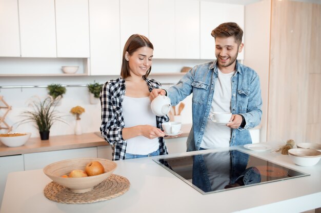 Giovane uomo felice e donna in cucina, colazione, coppia insieme al mattino, sorridente, tè