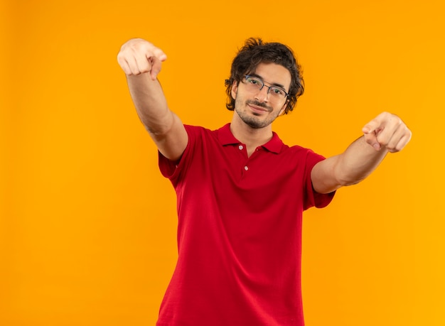 Giovane uomo fiducioso in camicia rossa con occhiali ottici punti con entrambe le mani isolate sulla parete arancione