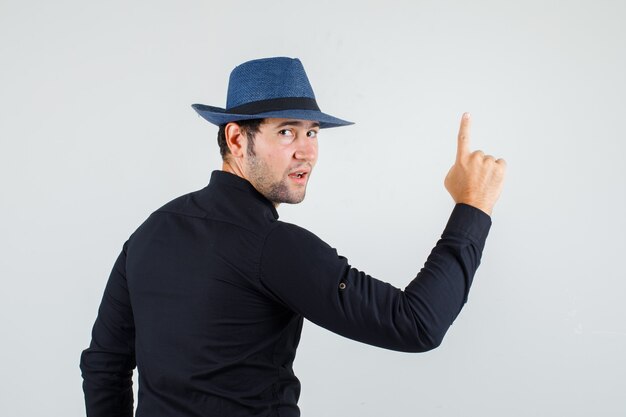 Giovane uomo guardando indietro e rivolto verso l'alto in camicia nera, cappello e guardando fiducioso.