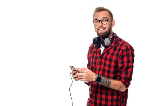 Giovane uomo hipster in camicia a scacchi e occhiali che indossano auricolari che sembrano felici su sfondo bianco. Studio girato. Copia spazio